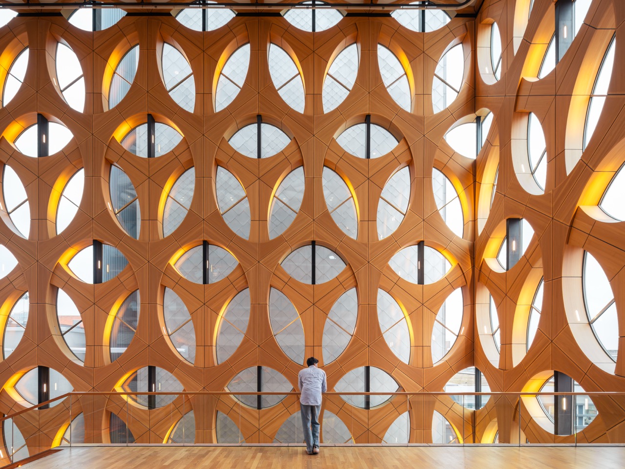 A figure at the railing of a vast timber lattice facade